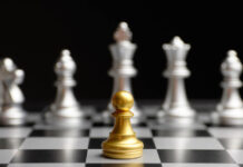 Chess photo. A gold pawn faces against a line of silver pieces