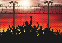 Enraged crowd of people are behind bars. Fence wire mesh barbed wire, vector silhouette. Street camera on the pillar. Sunset background.