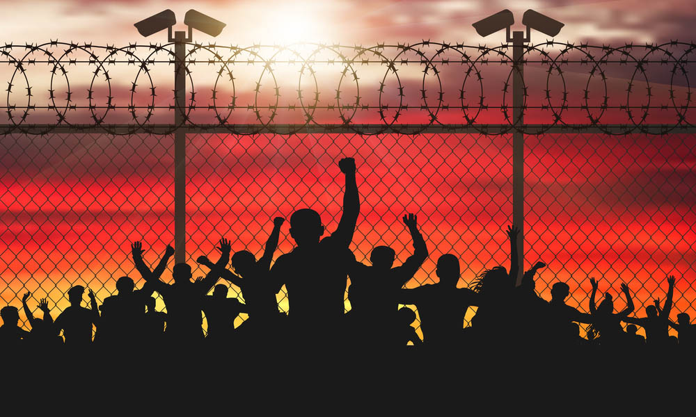 Enraged crowd of people are behind bars. Fence wire mesh barbed wire, vector silhouette. Street camera on the pillar. Sunset background.
