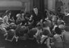 BW photo. Man in a suit telling children