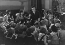 BW photo. Man in a suit telling children