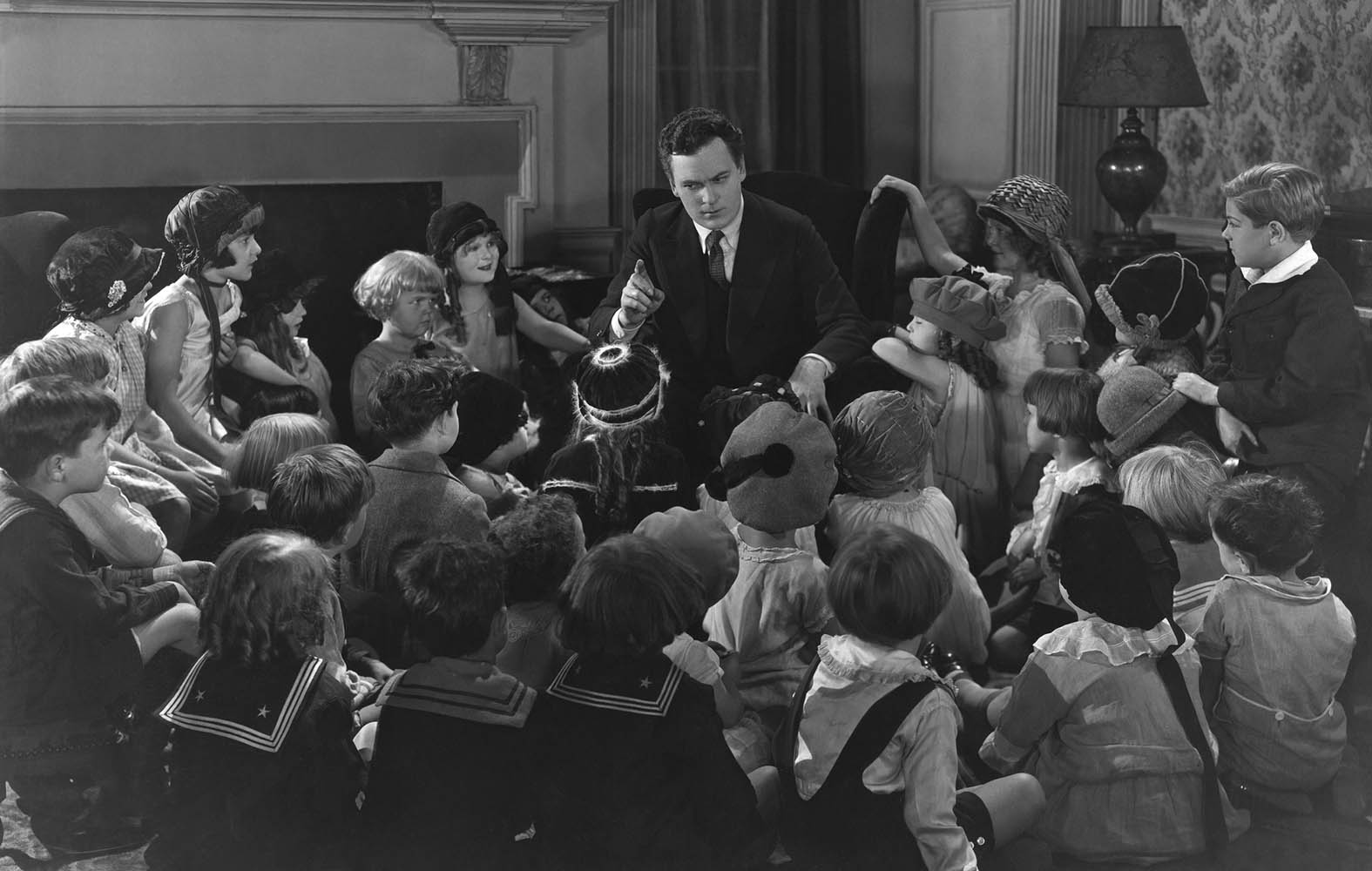 BW photo. Man in a suit telling children