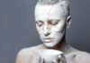 Close-up of a person covered in white paint with gold cracks, kintsugi style