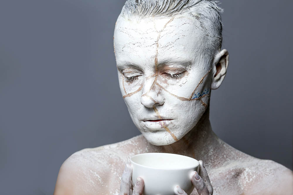 Close-up of a person covered in white paint with gold cracks, kintsugi style