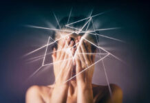 A person covers their face while white jagged lines emerge from their head