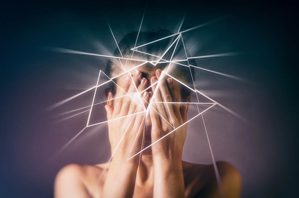 A person covers their face while white jagged lines emerge from their head