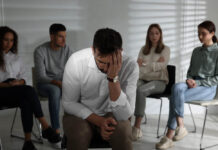 Unhappy man and group of people behind his back indoors. Therapy session