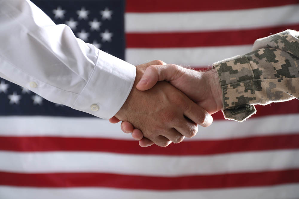 Soldier and politician shaking hands against flag of USA, closeup
