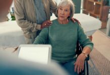 An elderly woman in a wheelchair tells a doctor (out of focus) about her symptoms