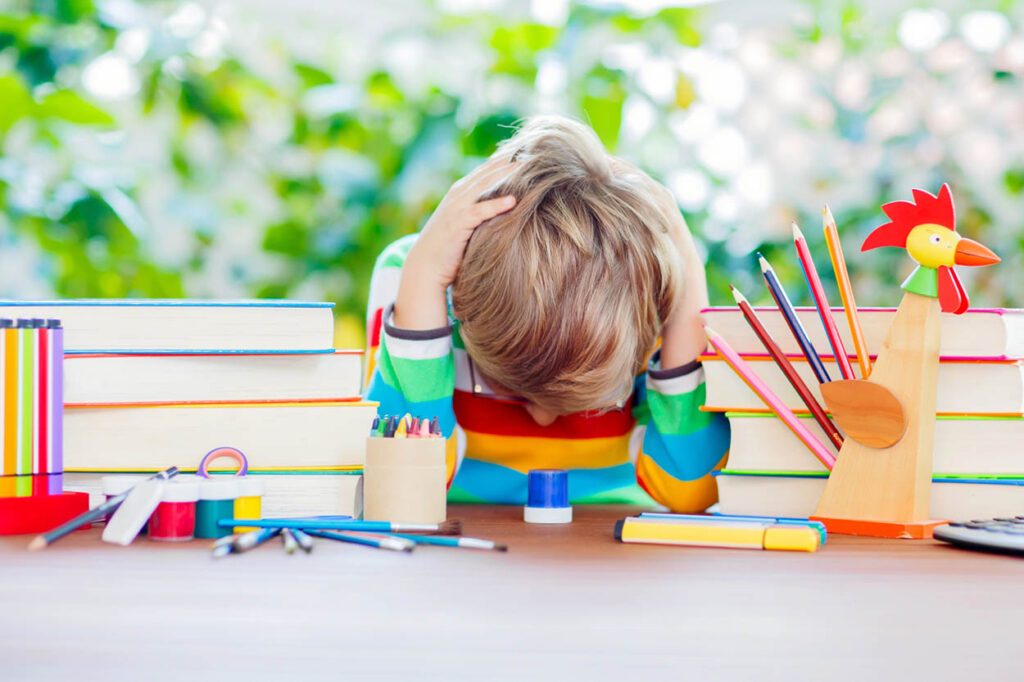 Child with head down on table with books and school supplies, bright colors