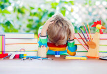Child with head down on table with books and school supplies, bright colors