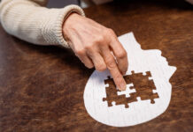 An elderly person's hand pushes a puzzle piece into a flat empty head shape