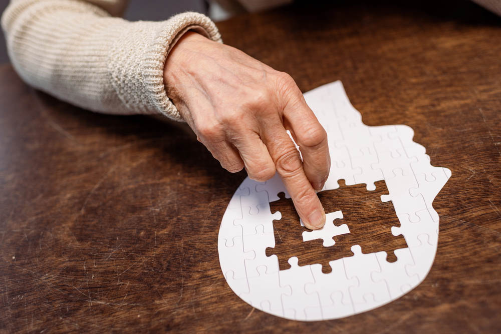 An elderly person's hand pushes a puzzle piece into a flat empty head shape