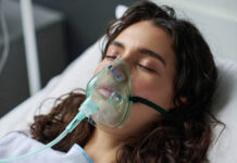 As a Doctor, I Felt Compelled to Agree to ECT—It Nearly Ruined My Life Close-up of young woman lying on bed with her eyes closed and breathing with oxygen mask in hospital