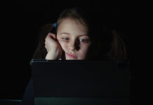 Is Focusing on Screen Time Diverting Us From the Real Drivers of Youth Distress? A child stares at a tablet in the dark
