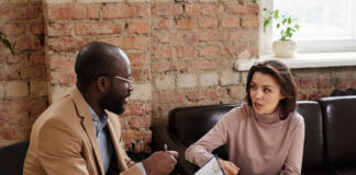 Beyond Medication: What England’s Experience Can Teach Us About Psychosis Care African-American psychologist in eyeglasses sitting with clipboard and working with problems of patient in loft office