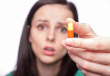 A Story of Bad Science: How Defenders of Antidepressant Efficacy Make Their Case Woman out of focus holding pill toward camera