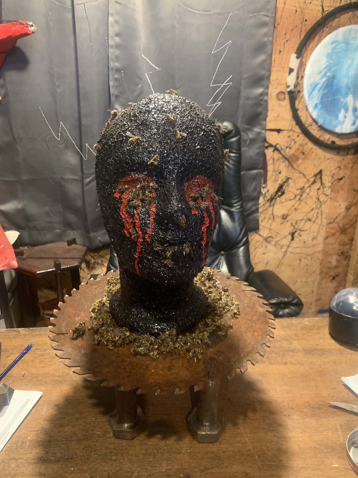 A sculpture of a head painted black sitting atop a saw blade on legs.